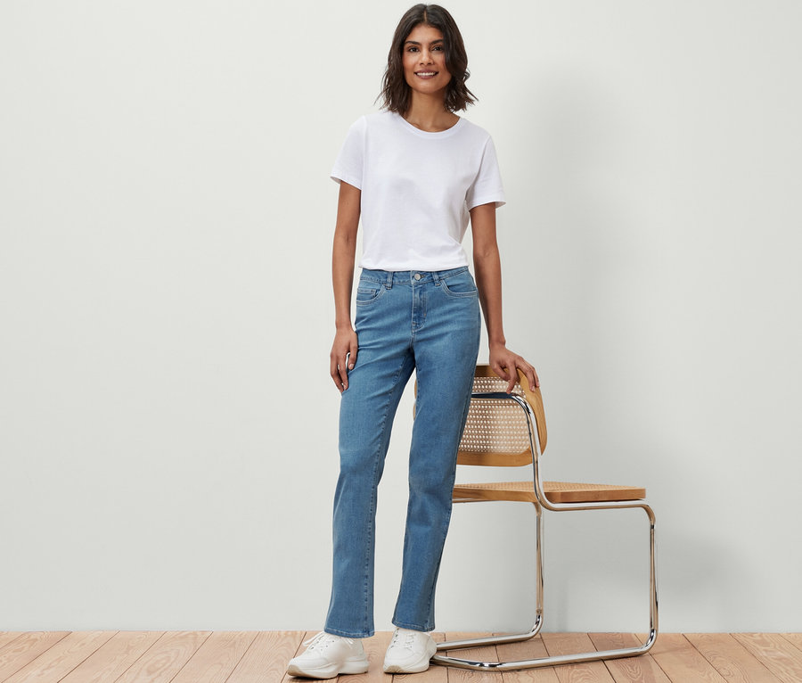 Eine Frau in einem weißen T-Shirt und Straight Jeans ‒ Fit »Kira« steht neben einem Stuhl.