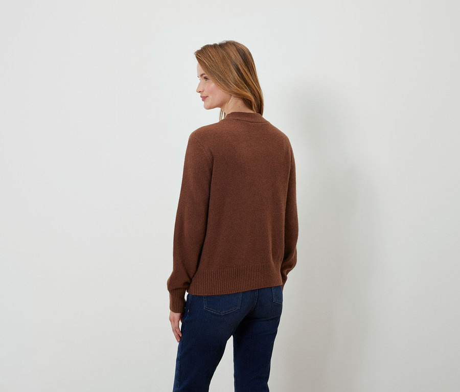 Rückansicht einer Frau mit braunen Haaren in einem braunen Pullover und dunkelblauen Jeans.