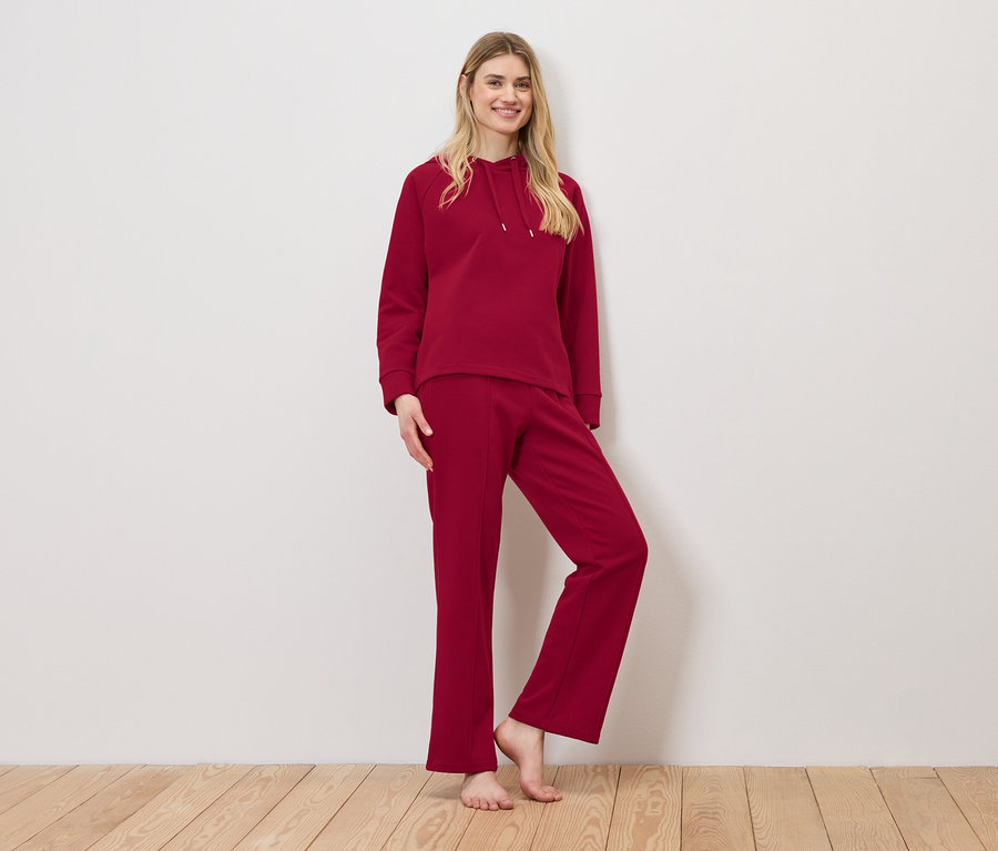 Eine Frau posiert in einem roten Trainingsanzug, bestehend aus einem Kapuzenpullover und einer Trainingshose.