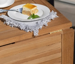 Ein Stück Kuchen auf einem Teller mit einer Tasse Kaffee auf dem deVries Balkontisch aus Teak.