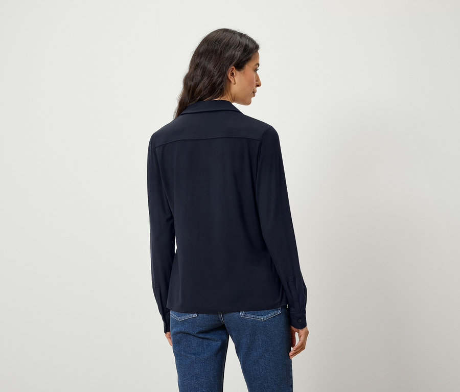 Rückansicht einer Frau mit dunklen Haaren in einem blauen Hemd und Jeans.