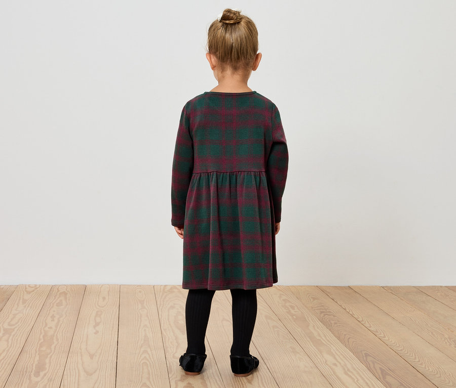 Mädchen in einem karierten Kleid steht mit dem Rücken zur Kamera.