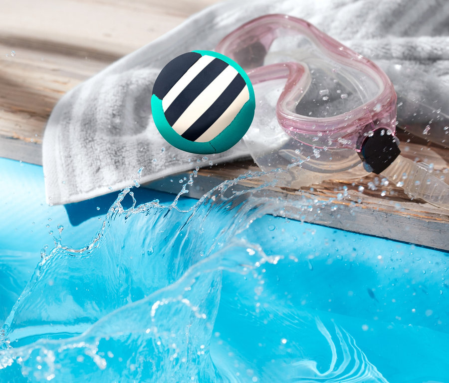 Hüpfender Wasserball landet im Pool neben Handtuch und Brille.