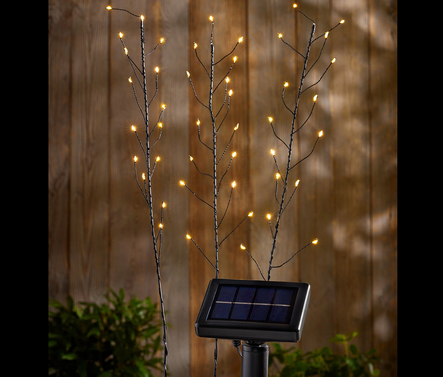 Drei Solar-Spieße mit LED-Lichtern vor einer Holzwand.