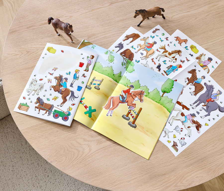 Ein geöffnetes Stickerbuch »Pferde und Ponys« liegt auf einem Tisch, daneben zwei Pferdefiguren.