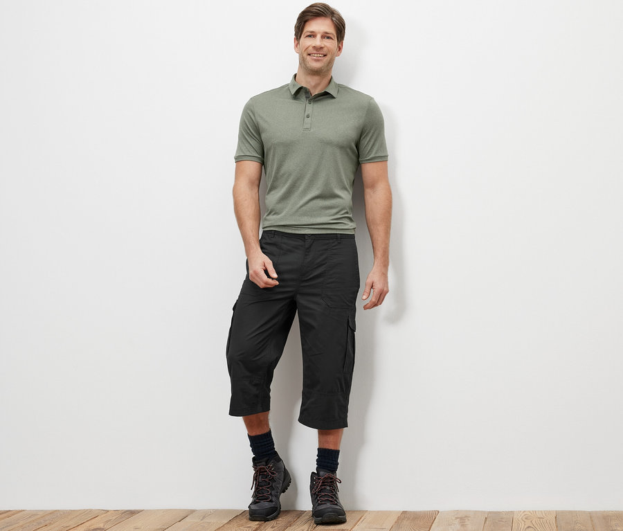 Ein Mann steht und trägt ein grünes Poloshirt und eine anthrazitfarbene Cargo-Bermuda in 3/4-Länge.