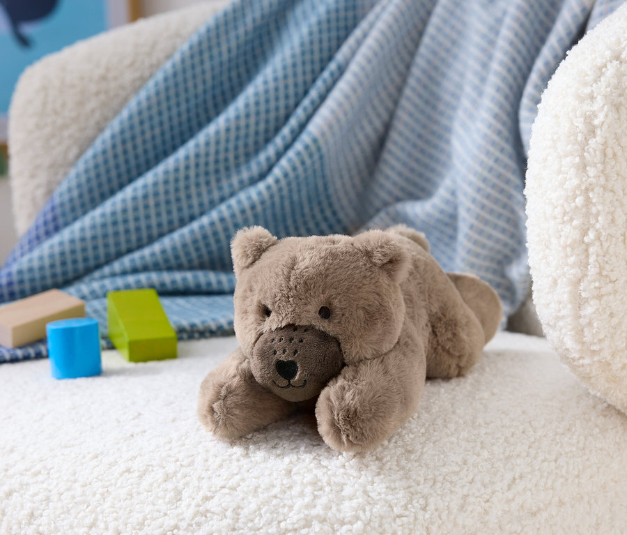 Ein brauner Teddybär liegt auf einem weißen, flauschigen Sessel neben Holzbausteinen.