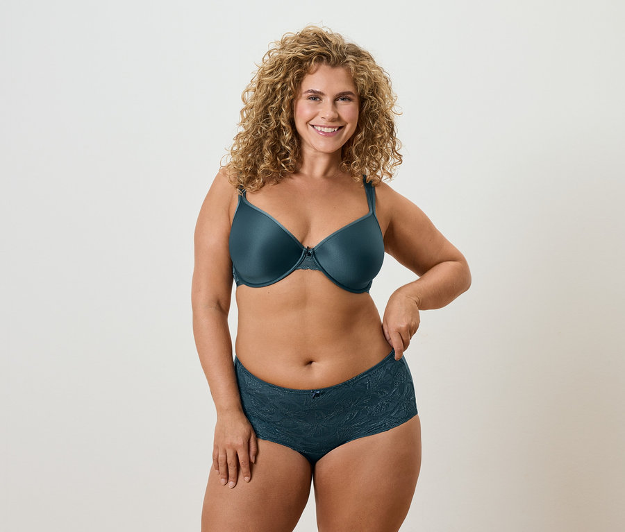 Frau mit lockigen blonden Haaren, die einen petrolfarbenen BH und dazu passende Unterwäsche trägt.