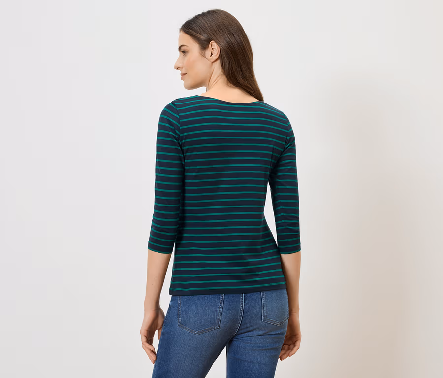 Eine Frau von hinten, mit braunen Haaren, trägt ein blau-grün gestreiftes Shirt und Jeans vor einem weißen Hintergrund.