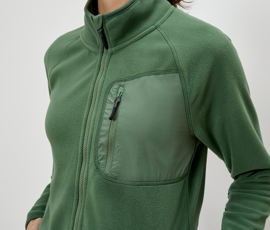 Nahaufnahme einer Frau, die eine grüne Fleecejacke mit Reissverschluss und einer Brusttasche trägt.