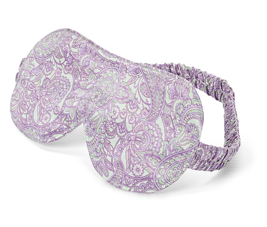 Nahaufnahme einer Schlafmaske mit lila Paisleymuster auf weißem Grund.