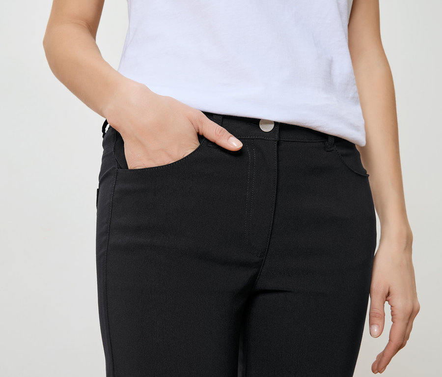 Frau mit Hand in der Tasche einer schwarzen Hose und einem weißen T-Shirt.
