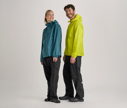 Frau in blaugrüner und Mann in hellgrüner Regenjacke und schwarzer Regenhose stehen nebeneinander vor hellem Hintergrund.