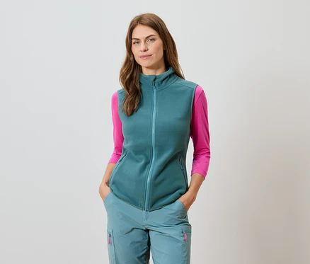 Frau mit petrolfarbener Weste und passender Hose mit pinkfarbenem Langarmshirt.