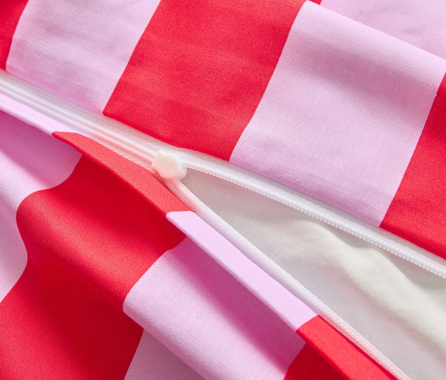 Nahaufnahme eines teilweise geöffneten Bettbezugs mit rot-rosa Streifen und einem weißen Reißverschluss.