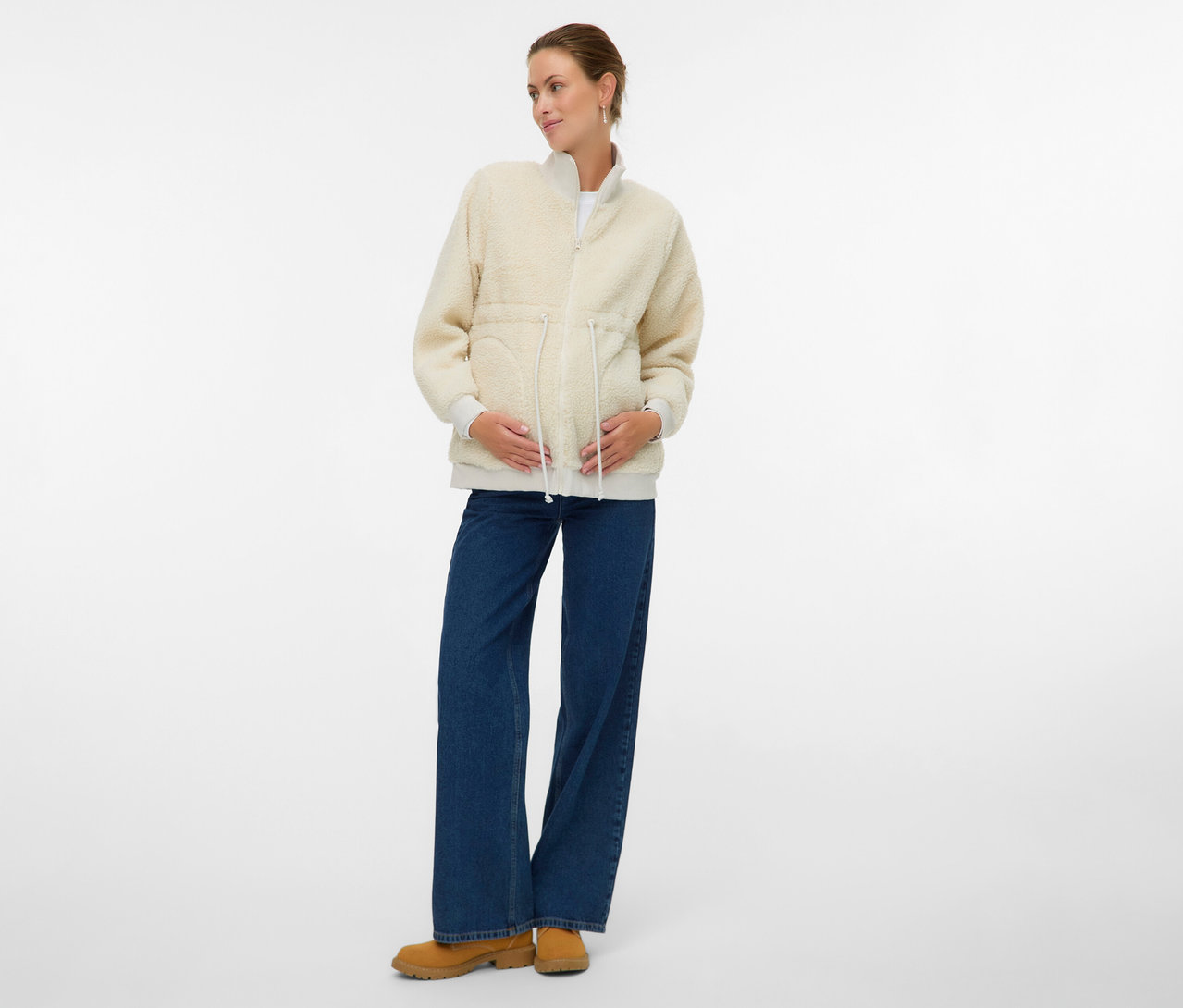 Schwangere Frau trägt die MAMALICIOUS 3-in-1-Teddyjacke »MLCARLY« über Jeans und Stiefeletten.