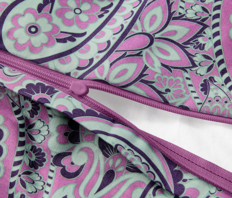 Nahaufnahme eines teilweise geöffneten Kissens mit Reißverschluss und Blumenmuster in Lila, Rosa und Grün.