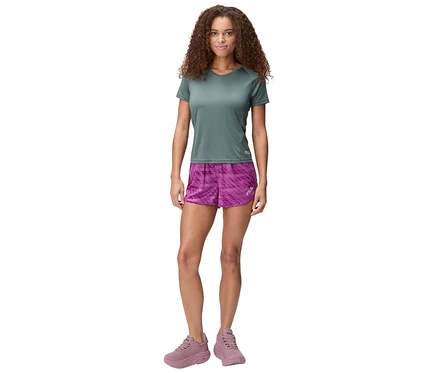 Frau mit lockigem Haar trägt ein graues T-Shirt, lila gemusterte FILA Damen-Funktionsshorts und rosa Turnschuhe.
