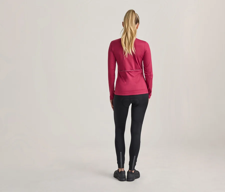 Frau von hinten, trägt ein pinkes langärmeliges Sportoberteil, schwarze Leggings mit reflektierenden Streifen und schwarze Sportschuhe.
