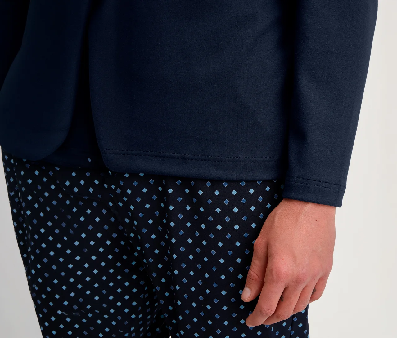 Nahaufnahme einer Person in einem marineblauen Langarmshirt und einer dunkelblauen Hose mit hellblauem Rautenmuster. Eine Hand ruht am Bein.