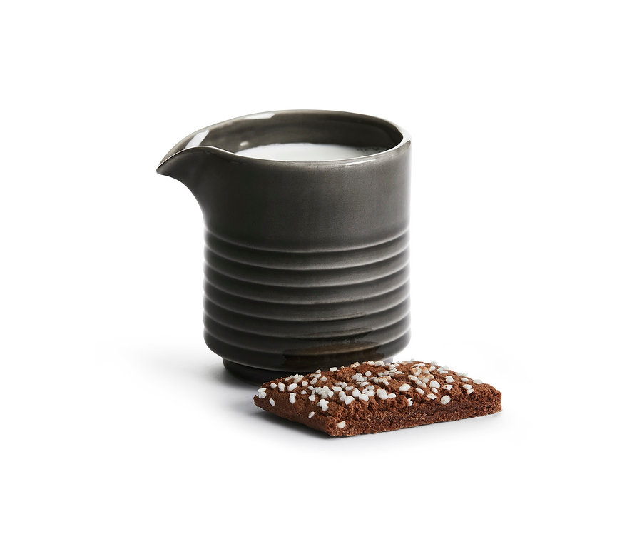 Ein graues Keramik-Milchkännchen neben einem Keks mit weißer Streusel.
