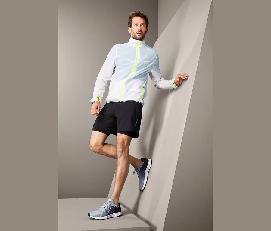 Mann posiert in Lightweight-Sportjacke, schwarzen Shorts und Turnschuhen.