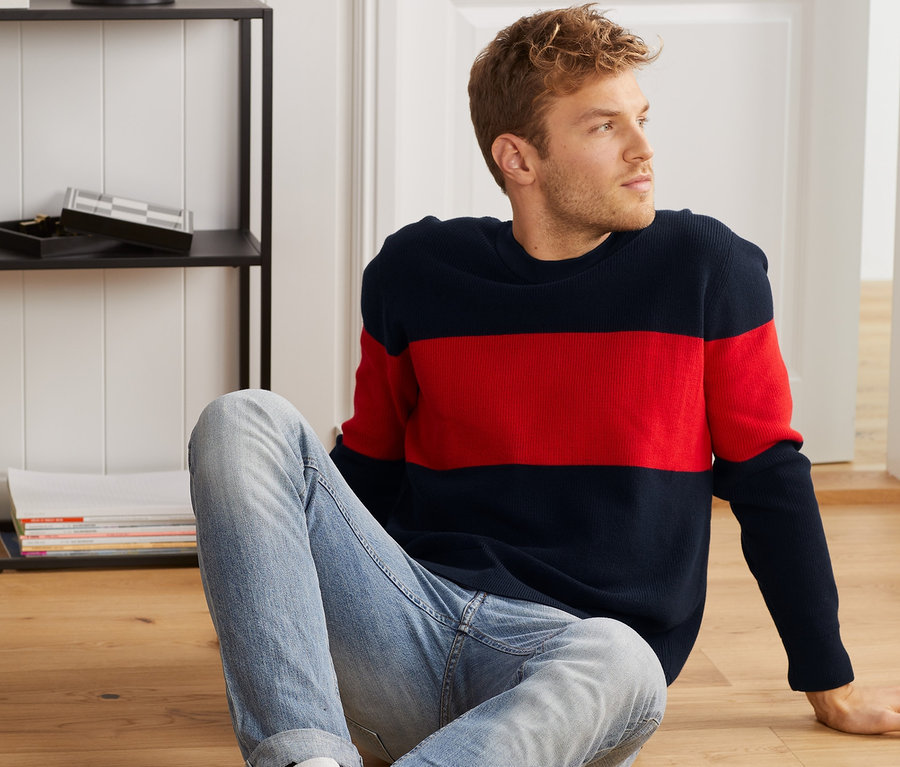 Mann sitzt auf dem Boden und trägt einen Strickpullover.