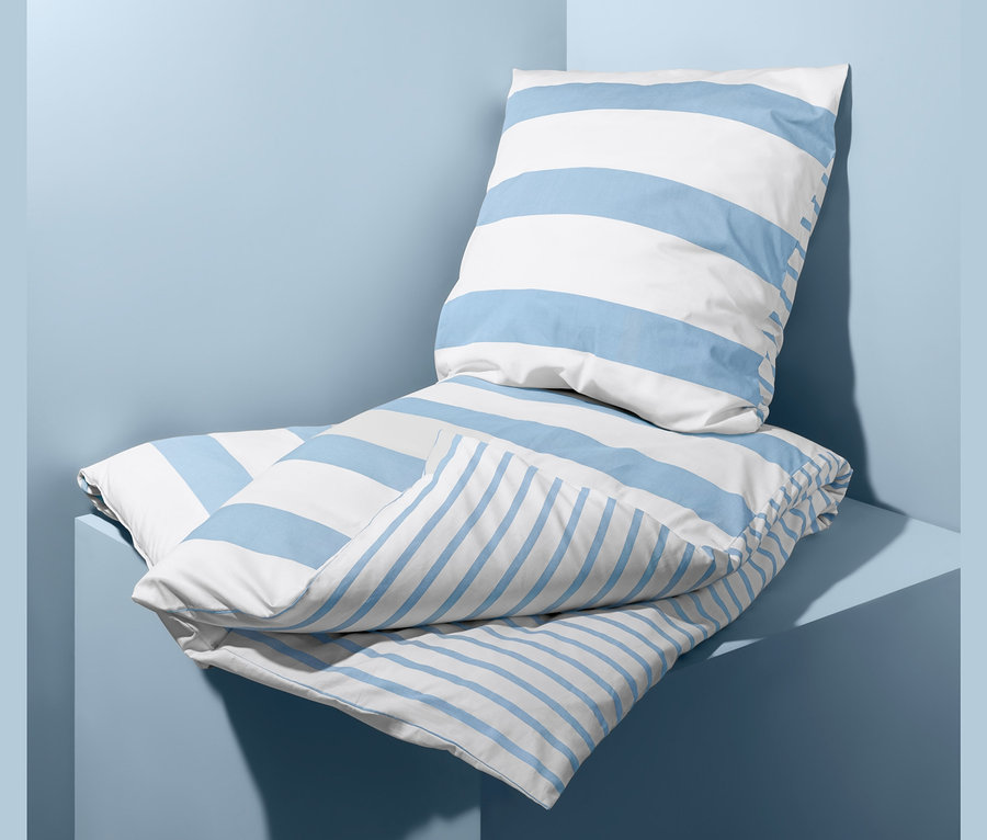 Auf hellblauem Hintergrund liegt ein Bettwäsche-Set mit blauen und weißen Streifen.
