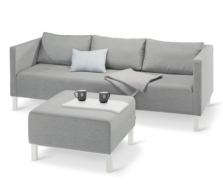 Hellesgraues Lounge-Sofa mit Sunbrella®-Stoff, Kissen und Decke, zwei Tassen auf einem grauen Hocker.