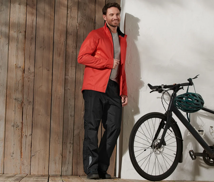 Mann mit roter Jacke und High-Tech-Regenhose steht neben einem Fahrrad.