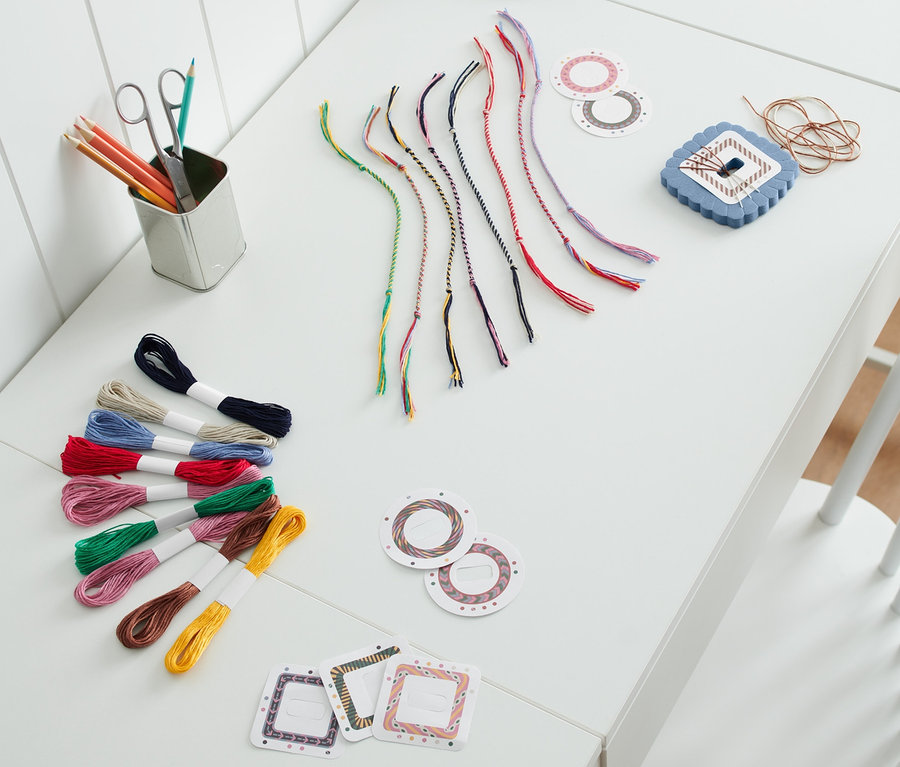 Auf einem weißen Tisch liegen ein Bastel-Set »Freundschaftsbänder«, bunte Fäden und eine blaue Lampe.