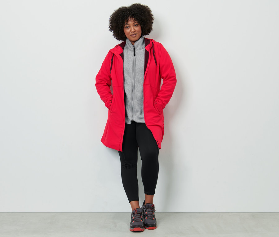 Frau trägt einen roten Softshellmantel, eine hellgraue Strickfleece-Jacke und eine Thermotight.