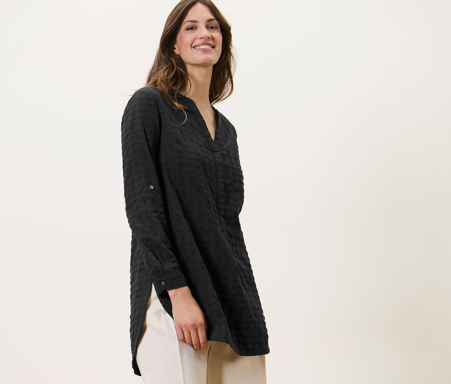 Frau trägt eine Longtunika mit Webstruktur und helle Hosen.