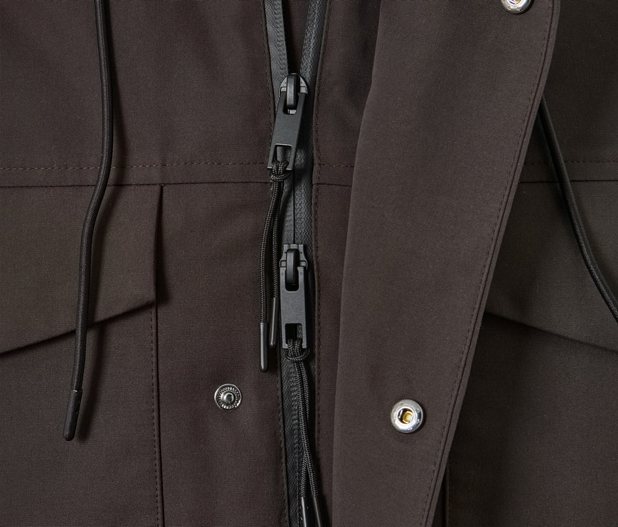 Detailaufnahme einer braunen Parka mit schwarzem Reißverschluss und silberfarbenen Druckknöpfen.