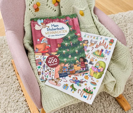 Auf einem Sessel liegt ein geöffnetes Weihnachtsstickerbuch mit Weihnachtsmotiven.