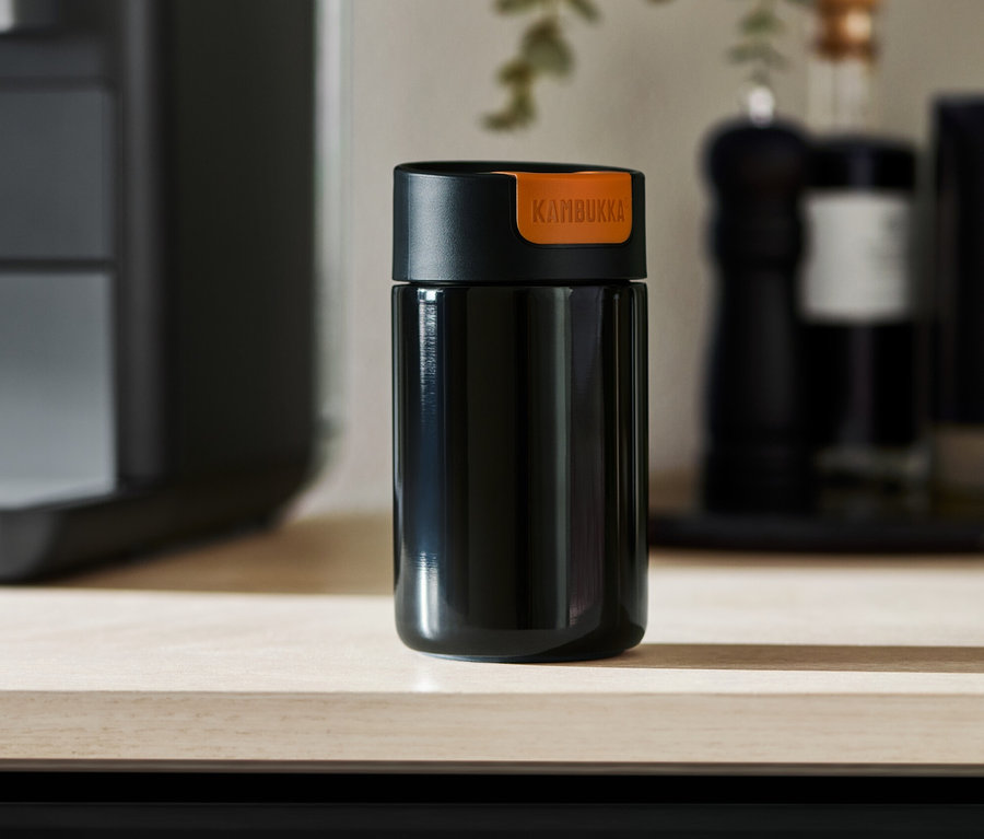 Ein schwarzer Kambukka To-Go-Becher steht auf einer hellen Tischplatte.