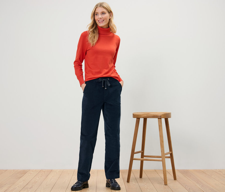Frau posiert in Cord-Joggpants und orangefarbenem Rollkragenpullover.