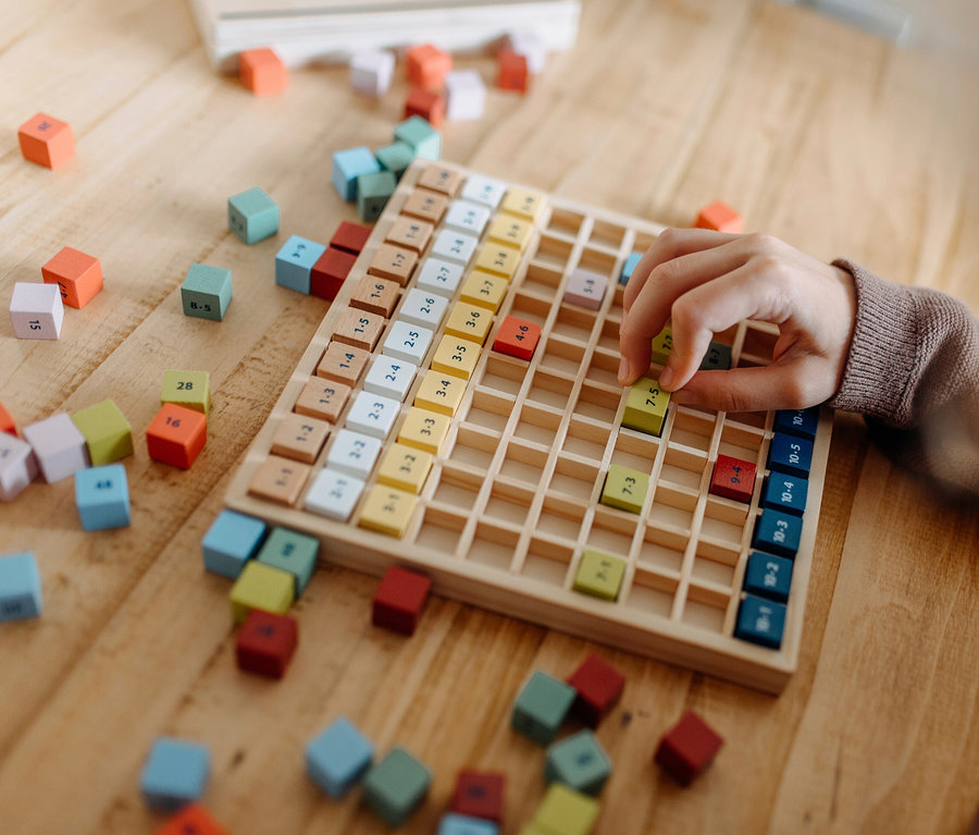 Kind spielt mit einem hölzernen small foot Rechen-Set »Educate« mit bunten Würfeln auf einem Holztisch.