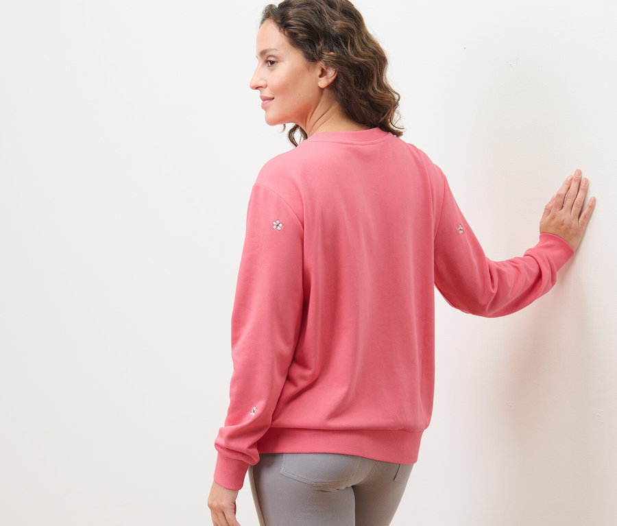 Frau trägt ein besticktes Sweatshirt und graue Hosen.
