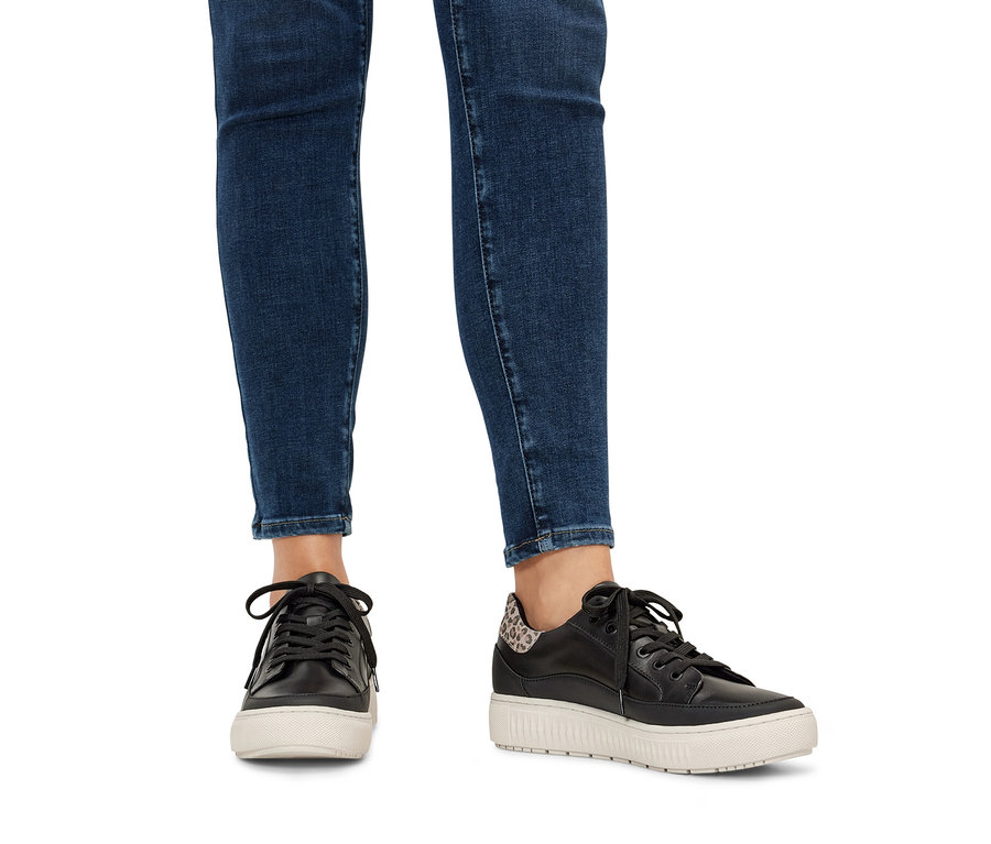 Beine in Jeans und Leder-Sneaker.