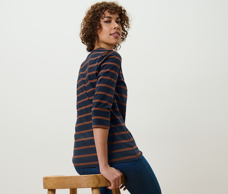 Frau sitzt auf einem Hocker und trägt ein gestreiftes Shirt mit 3/4-Arm.