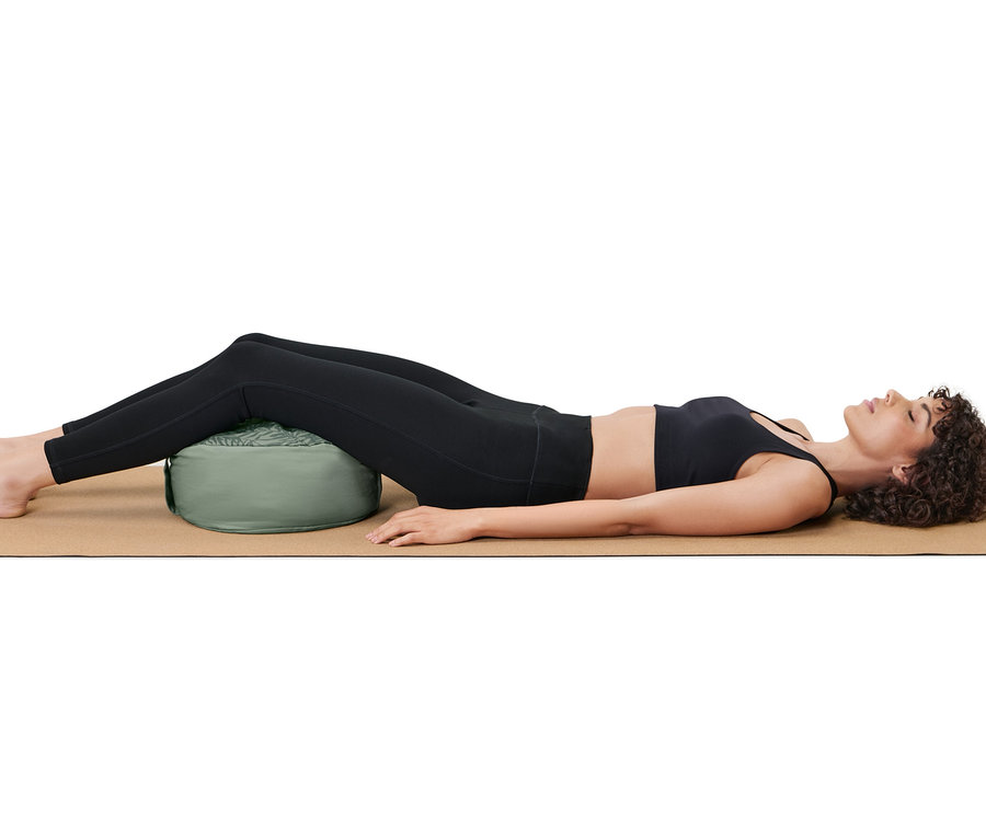 Frau liegt auf einer Matte, ein Meditationskissen unter ihren Beinen.