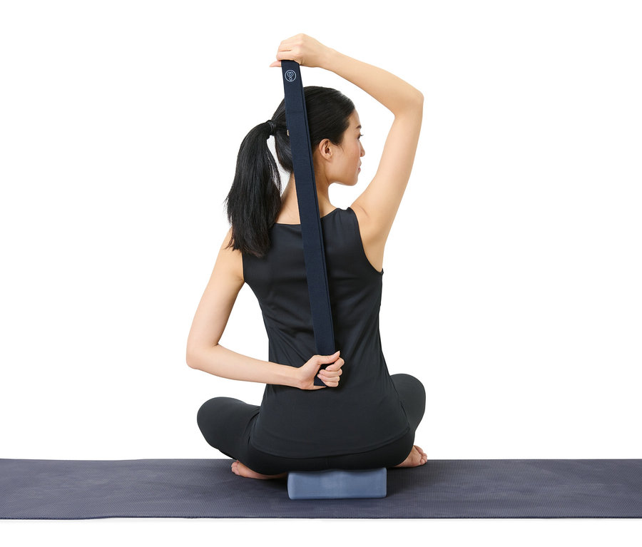 Frau sitzt auf Yogamatte und benutzt Yogagurt aus Yoga-Set.