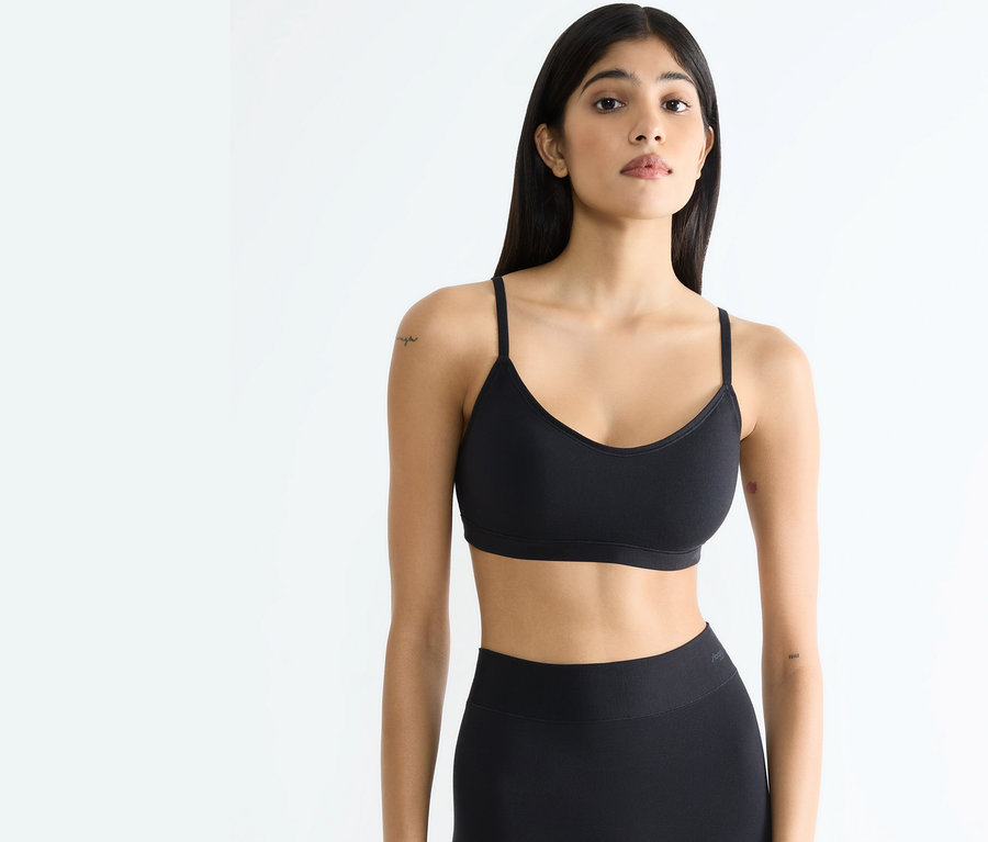 Frau in schwarzem Sporttop und Leggings posiert vor weißem Hintergrund.