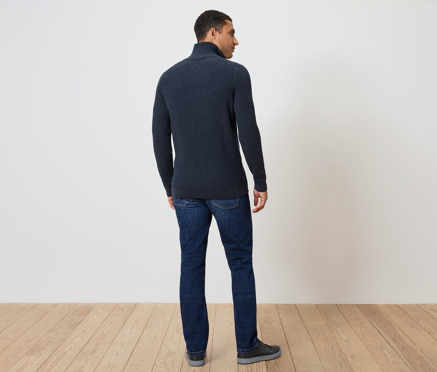 Ein Mann steht mit dem Rücken zur Kamera und trägt einen dunkelblauen Pullover und Jeans.