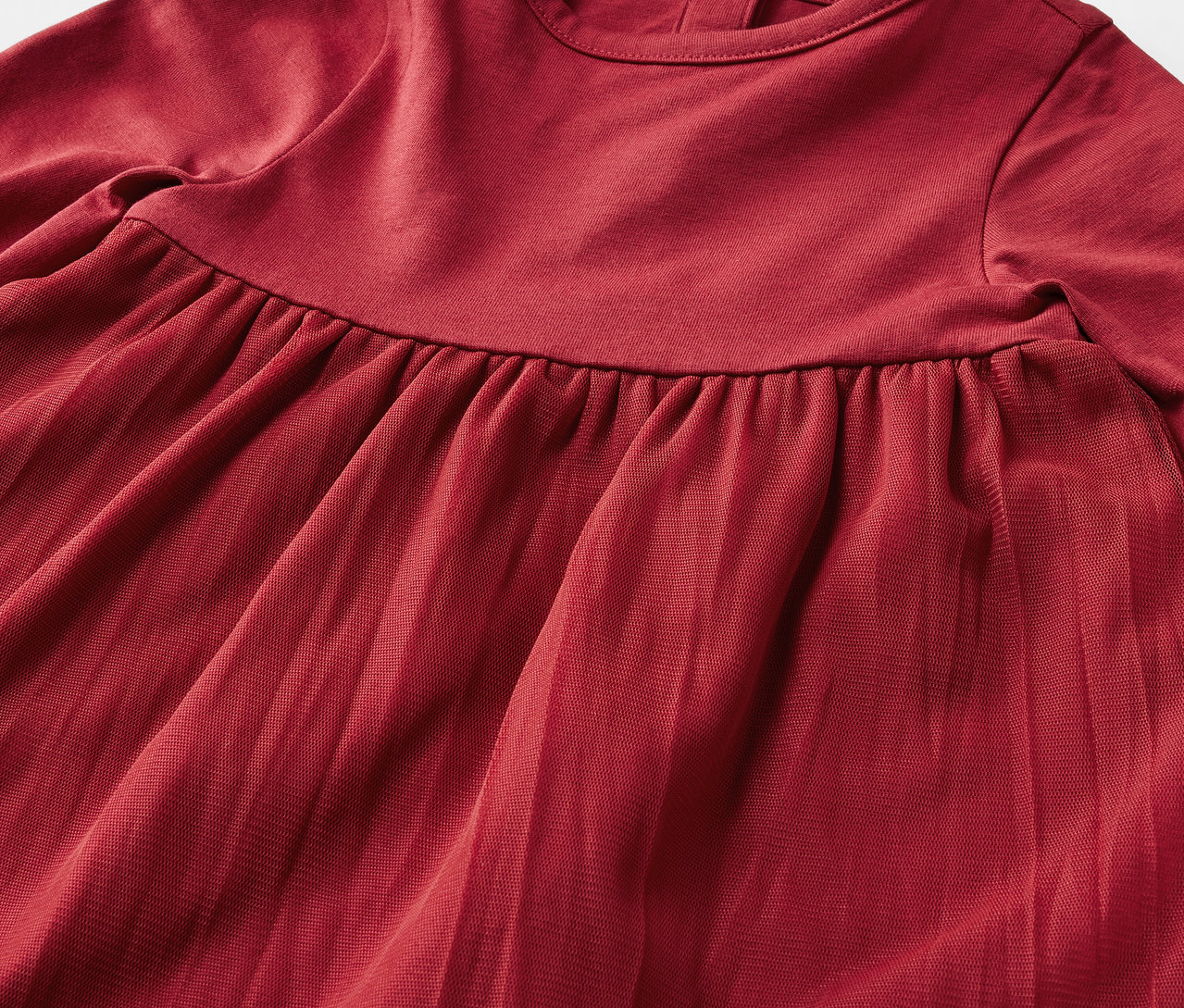 Detailaufnahme eines roten, langärmligen Kleides mit Faltenrock.
