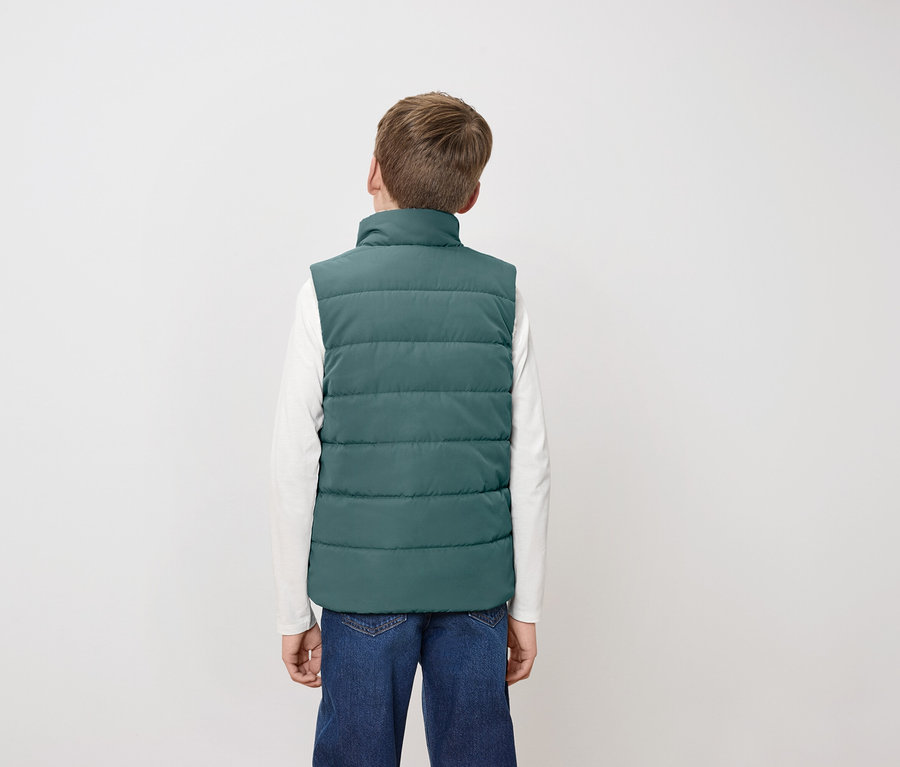 Junge mit dem Rücken zur Kamera trägt eine grüne Steppweste, ein weißes Langarmshirt und Jeans.