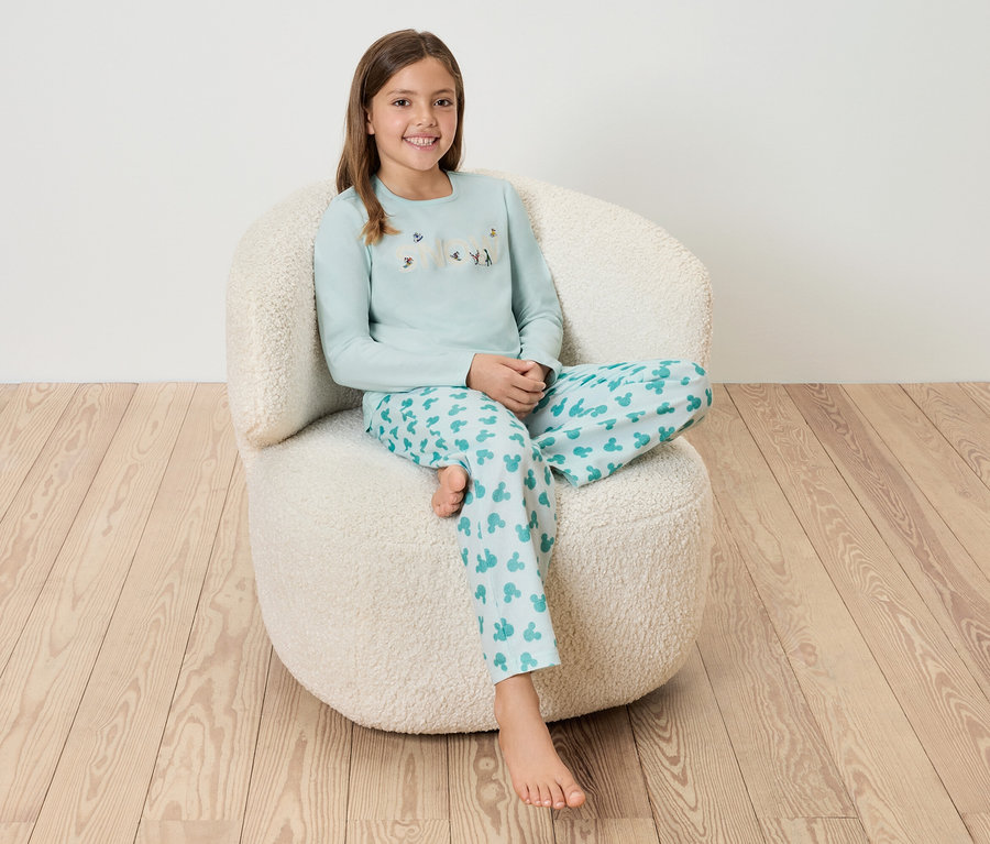 Mädchen sitzt in blauem Pyjama auf einem weißen, zotteligen Sessel.