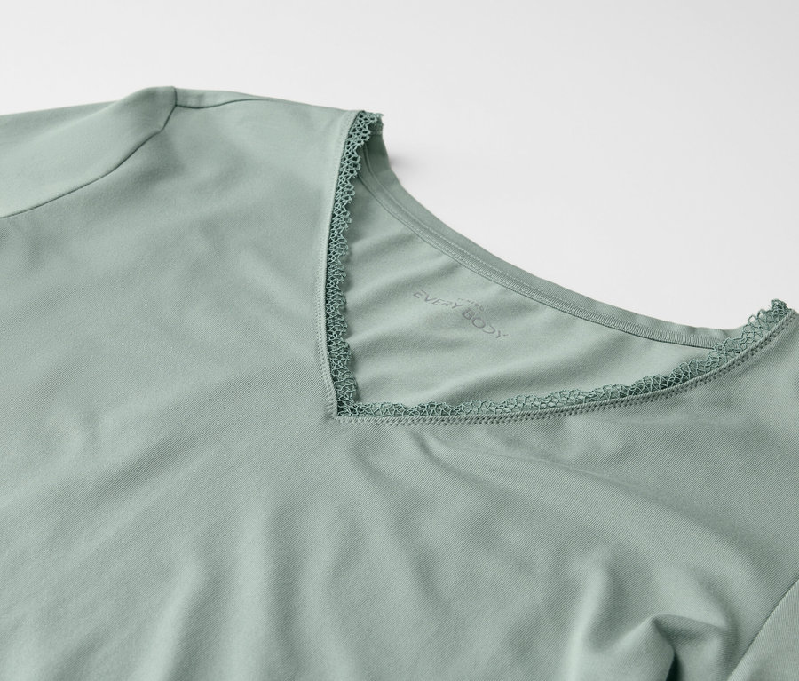 Detailansicht eines hellgrünen T-Shirts mit kurzen Ärmeln und einem V-Ausschnitt, der mit Spitze besetzt ist.