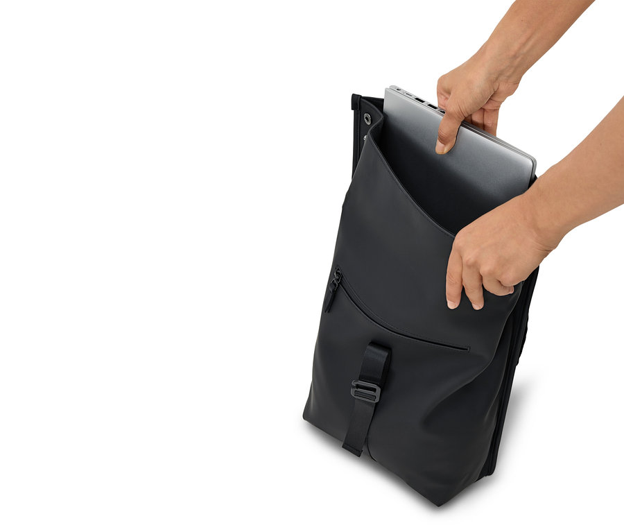 Hände legen einen silbernen Laptop in einen geöffneten schwarzen Rucksack.